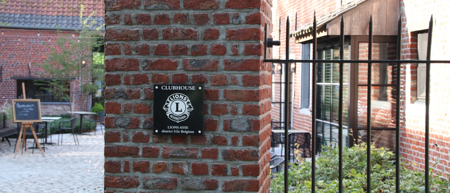 Plakkaatje 'Clubhouse Lions Asse - district 112c Belgium' aan de ingang van restaurant Eenhoorn te Asse